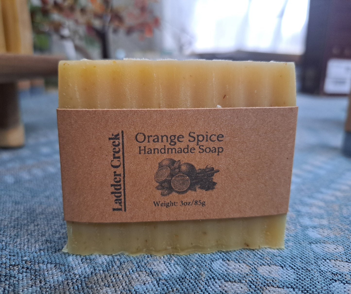 Bar of orange spice handmade soap with a brown cardboard box on a textured surface.