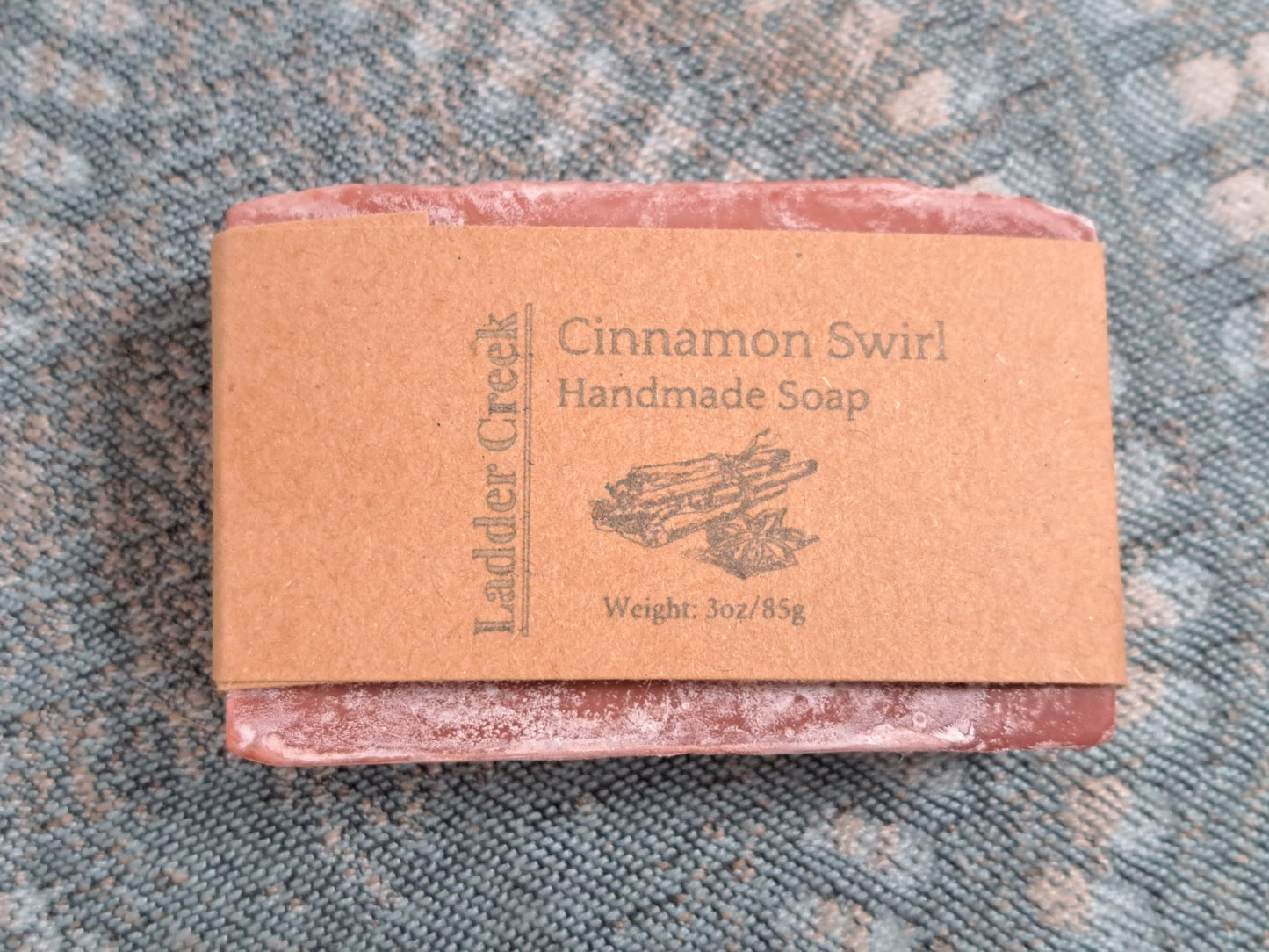 Bar of cinnamon swirl handmade soap with a brown label on a textured surface