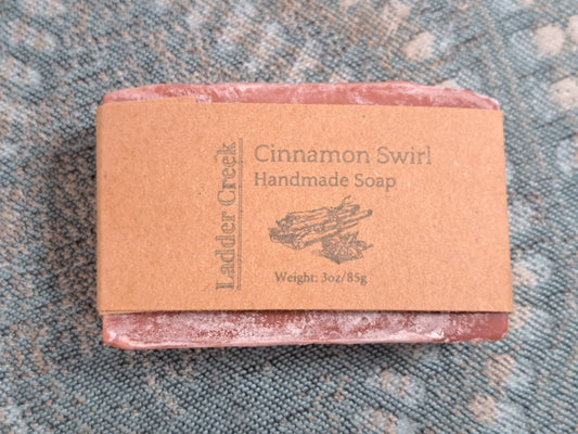 Bar of cinnamon swirl handmade soap with a brown label on a textured surface