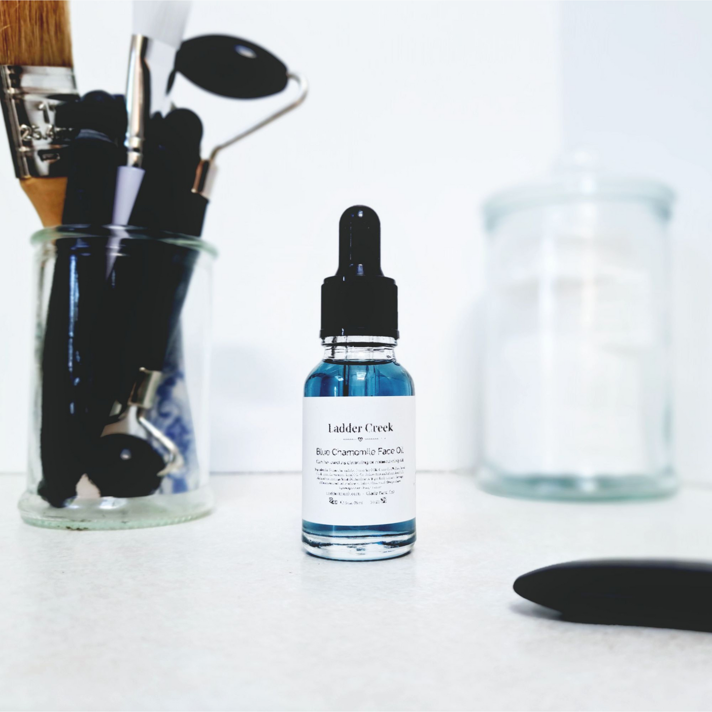 Bottle of Ladder Creek facial oil with makeup tools on a white surface