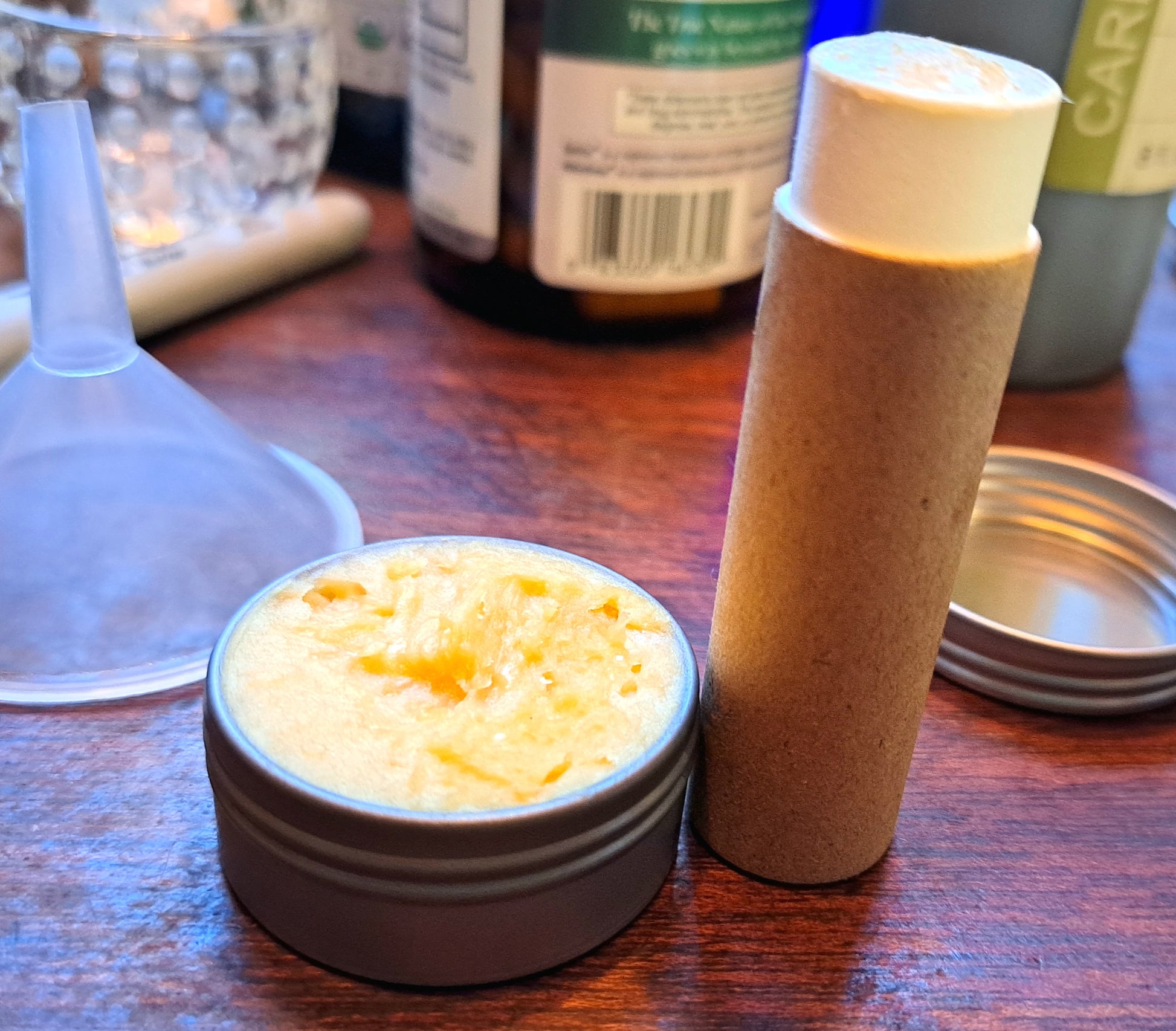 Small containers with lip balm. One a tin, next to a cardboard tube on a wooden surface.